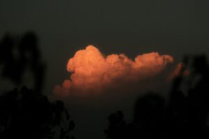 A single orange cloud illuminated by low sun against a dark sky